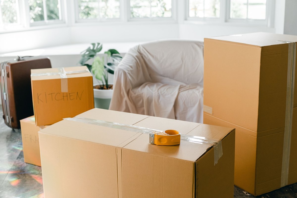 Taped moving boxes in front of a sheet-covered armchair by a bay window