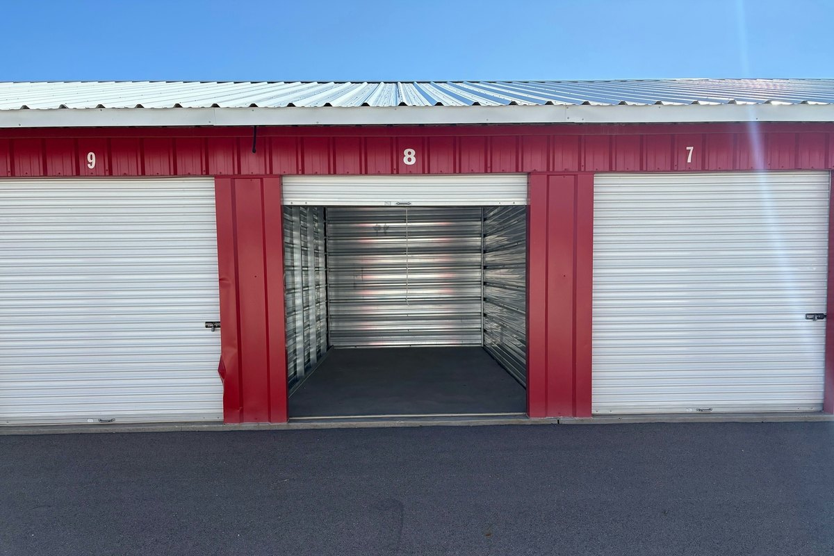 Storage building with red trim and one roll-up door open to an empty metal-walled unit