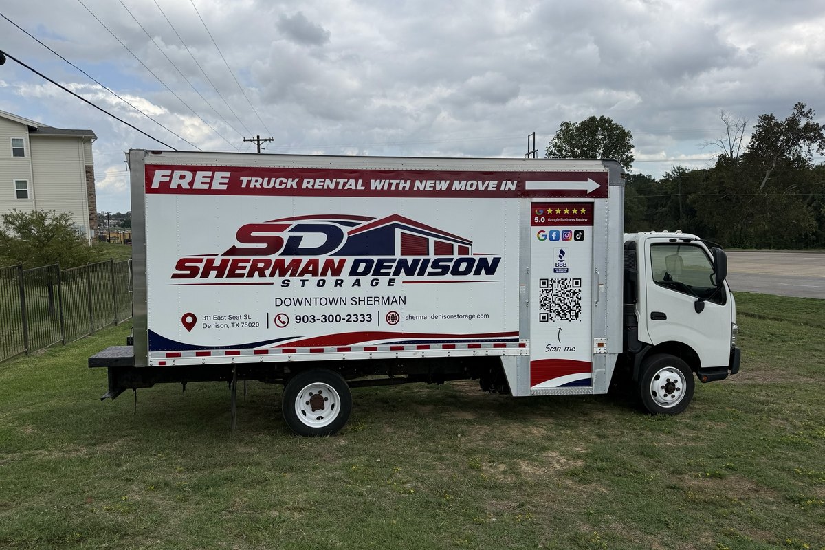 White box truck with a red band reading Free Truck Rental With New Move In, with a red and navy SD logo, on a lawn