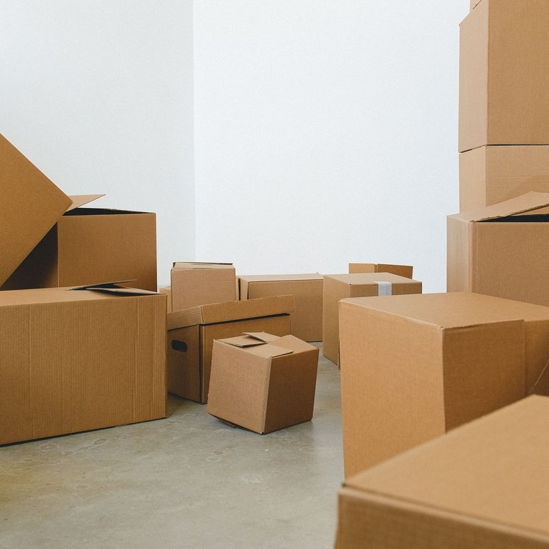 Brown cardboard boxes of many sizes piled in a bare white corner