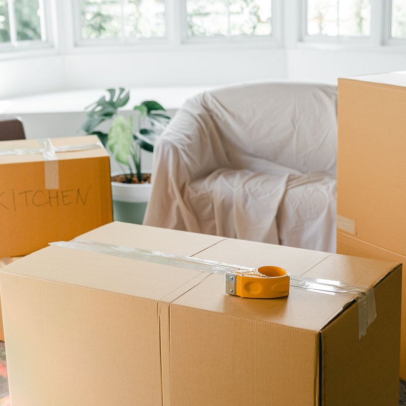 Taped cardboard moving boxes and a sheet-covered armchair in a sunlit room